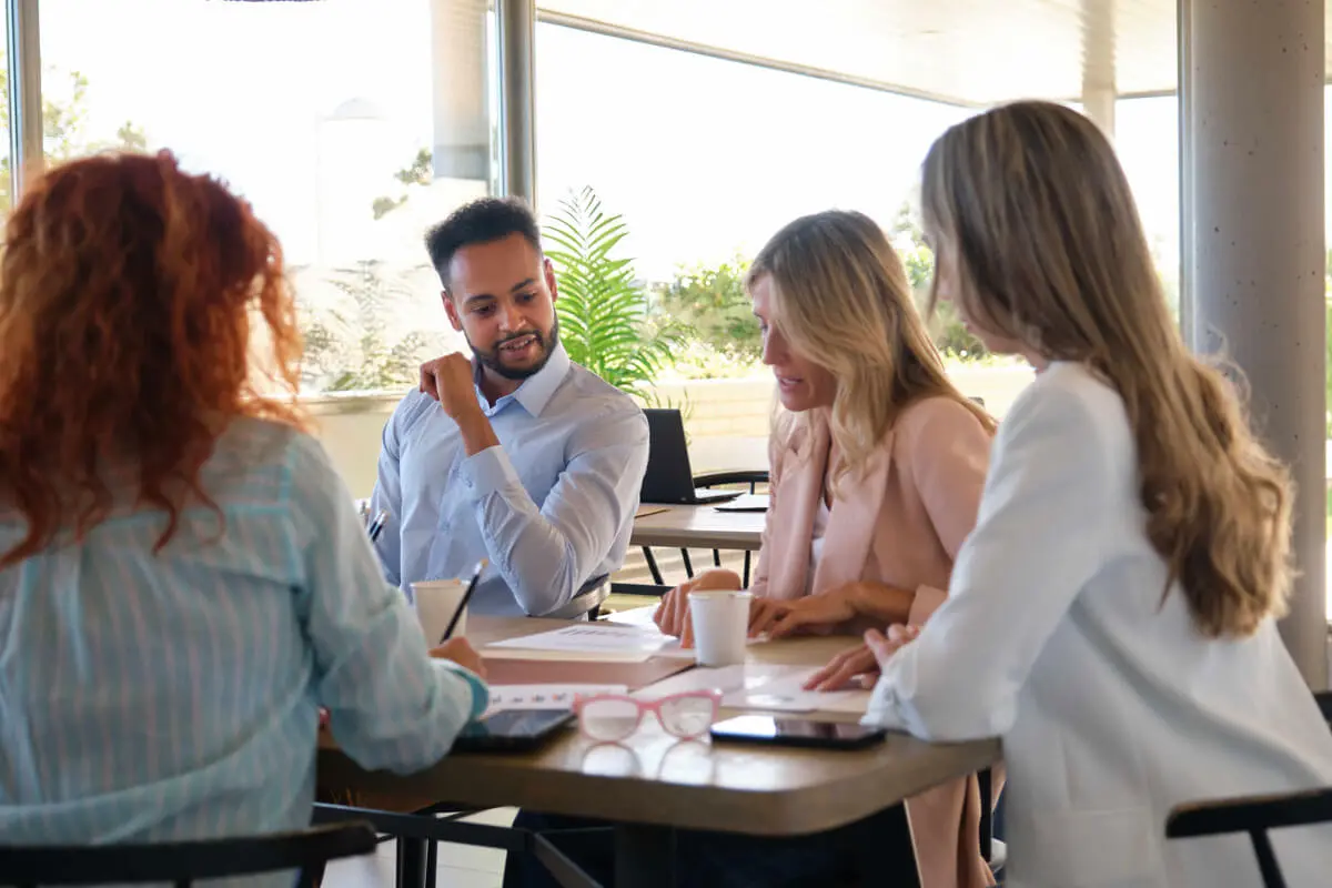 A group of people sitting at a table, engaged in conversation and providing nursing support to one another.